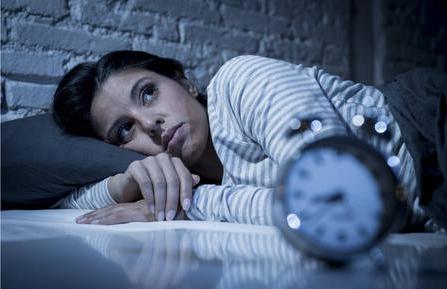 Woman laying in bed next to a clock.